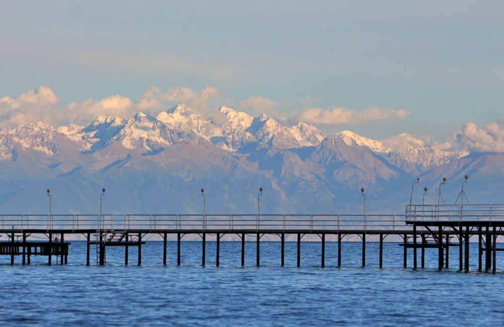 Info Shymkent - Sea bridge at Lake Issyk Kul with snow-capped Tienshan Mountains in the background