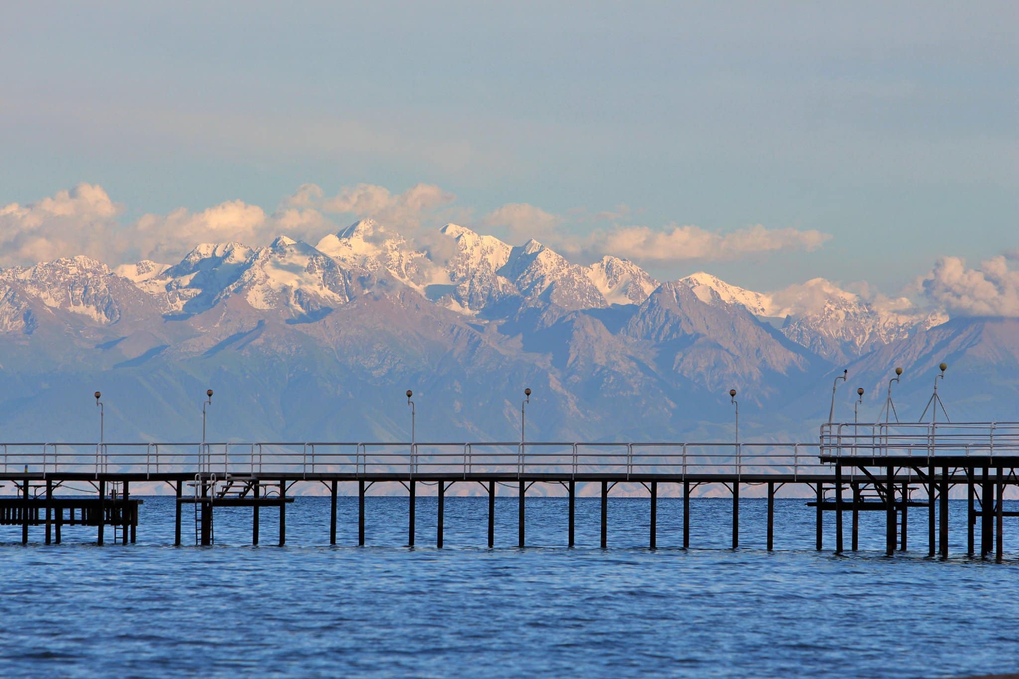 Info Shymkent - Sea bridge at Lake Issyk Kul with snow-capped Tienshan Mountains in the background