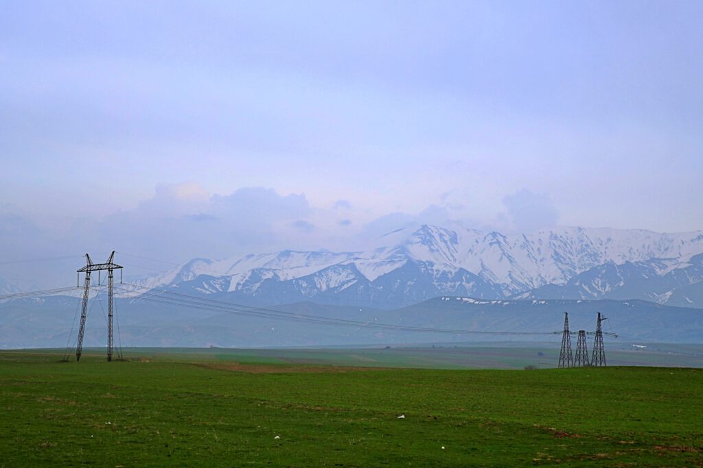 Info Shymkent - Power poles and green fields with Sairam-Ugam Mountain Range in the background